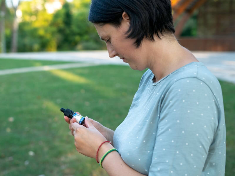 Vrouw buiten die naar een flesje CBD-olie van Formula Swiss in haar hand kijkt